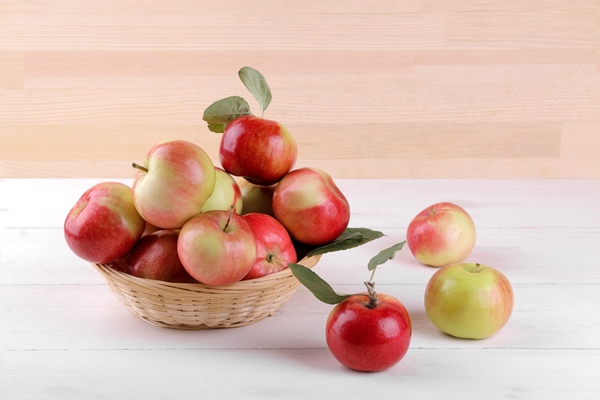 fresh ripe red apples with leaves in a basket on a white wooden table and on a background of natural wood - Закуска из свёклы, яблок и редиса