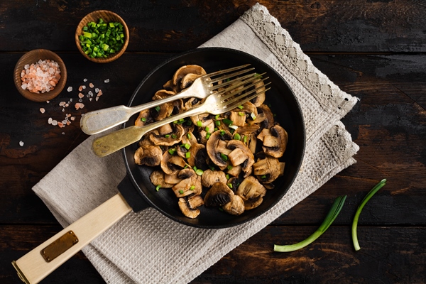 fried champignon mushrooms in a cast iron old pan on an old dark wooden rustic for frying - Постные макароны с грибами
