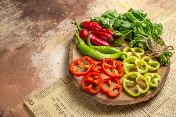 front view different vegetables coriander hot peppers bell peppers cut into pieces on round tree wood board a newspaper on amber background with copy space - Салат овощной с кунжутом и гранатом