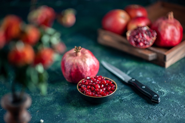 front view pomegranate seeds bowl knife pomegranates on wood board on dark surface - Салат фруктовый со шпинатом и гранатом