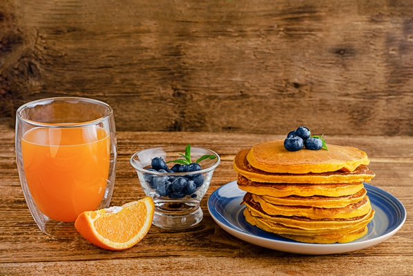 heap of pumpkin pancakes with blueberries and orange juice on rustic wooden table copy space - Морковные оладьи
