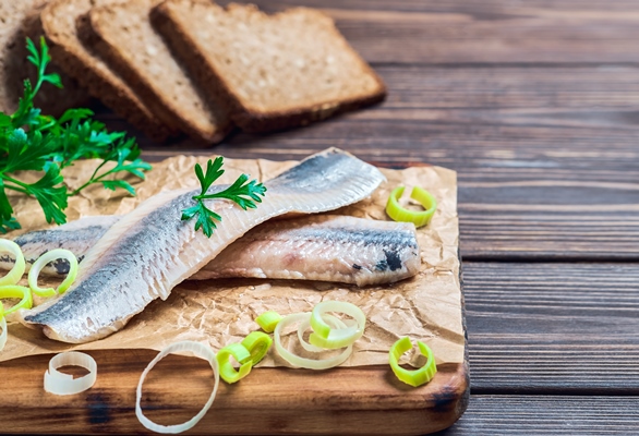 herring fillet with parsley and onion on a cutting board close up dark wooden background traditional norwegian or danish smorrebrod ingredients herring sandwich healthy food concept - Малосольная селёдка домашняя с луком