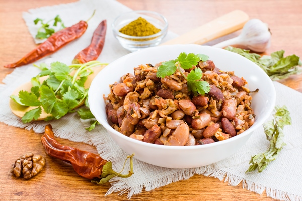 lobio the national georgian dish of beans in a white plate and the ingredients for its preparation on a wooden table - Постные фаршированные шампиньоны