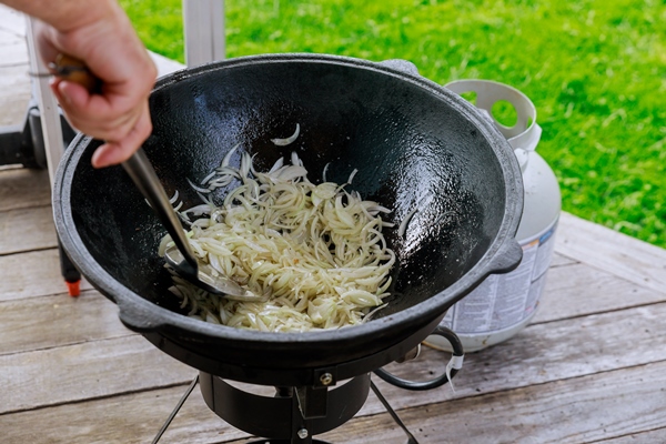 man fries and turns the onion in cauldron on fire - Жареный репчатый лук