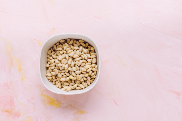 pine nuts in bowl on pink background with copy space - Постный салат с мандаринами