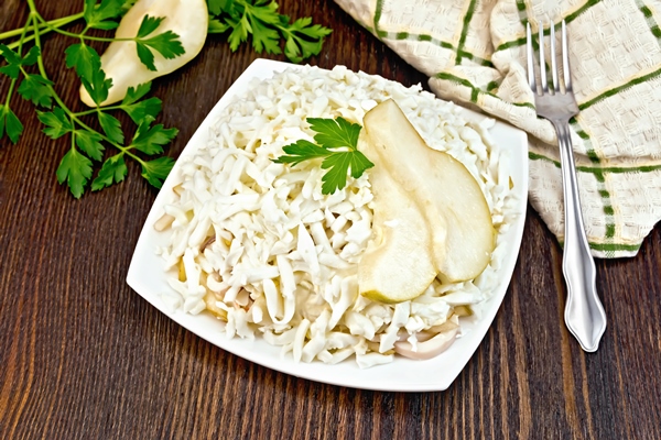 salad of squid rice pears and eggs in a plate parsley kitchen towel and fork on the background of wooden boards - Постный салат из кальмаров
