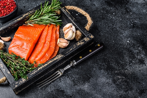 smoked sliced salmon fillet in a wooden tray with herbs black background top view copy space - Постные канапе с авокадо и лососем