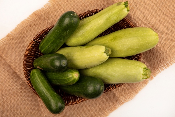 top view of green vegetables such as cucumbers zucchinis on a bucket on a sack cloth on a white wall - Салат из огурцов и цукини