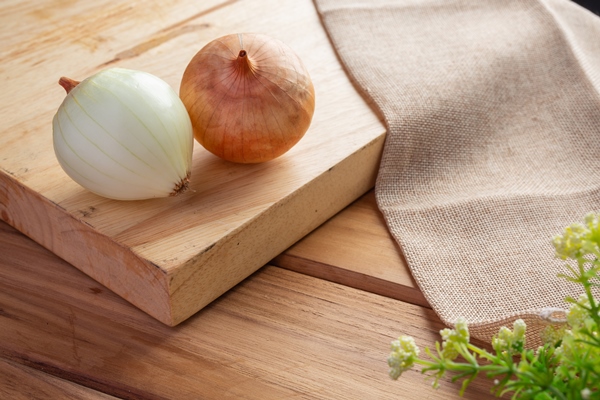 two onions on a light brown wood cutting board - Салат овощной с кунжутом и гранатом