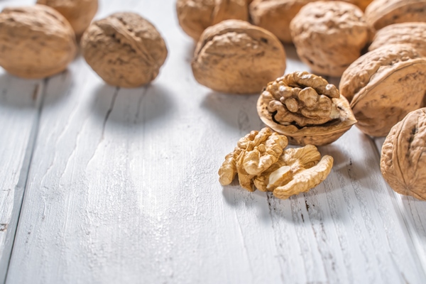 walnuts kernels on white wooden desk with place for text pile of whole walnut shells - Салат с грушей, орехами, шпинатом и тофу