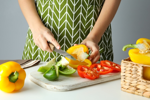 woman hands cut bell pepper on white board - Салат с перцем и хлебом