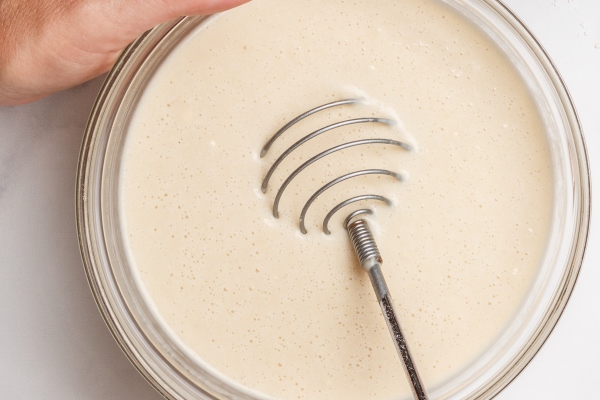 woman prepares dough for homemade pancakes for breakfast whisk for whipping in hands - Овсяные постные оладьи