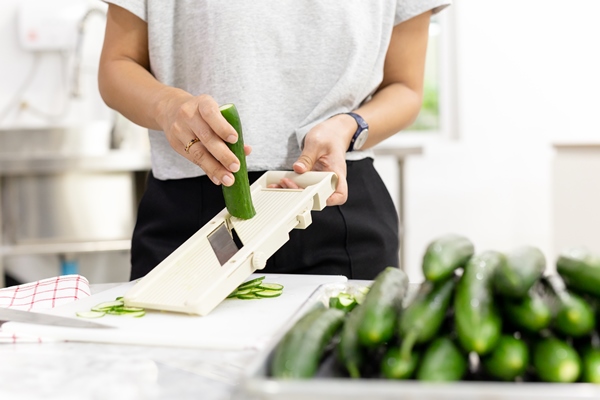 woman slicing cucumber with vegetable slicer for salad - Гаспачо