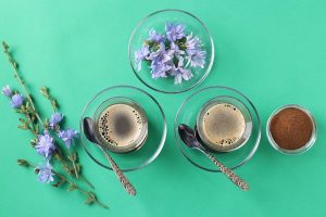 chicory beverage in two glass cups with concentrate and flowers on green - Напиток из цикория с пенкой