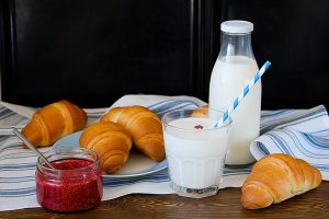 croissants on a plate raspberry jam milk in a bottle and in a glass on a wooden table - Розовый горячий шоколад