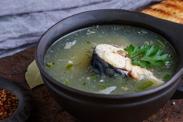 fish soup of mackerel in a brown clay plate on a wooden board - Уха осветлённая