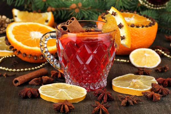 fragrant mulled wine in glass with spices and oranges around on wooden table - Безалкогольный глинтвейн с фруктово-ягодным соком