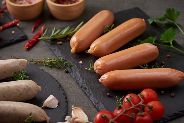 fresh raw sausages and ingredients for cooking classic boiled meat pork sausages on chopping board with pepper rosemary herbs and spices - Сосиски в слоёном тесте
