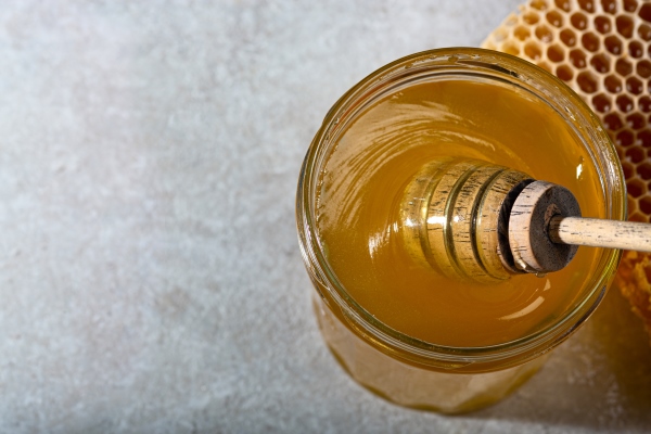 honey background sweet honey in the comb glass jar and a spoon for honey on the table light background banner - Безалкогольный глинтвейн с клюквой