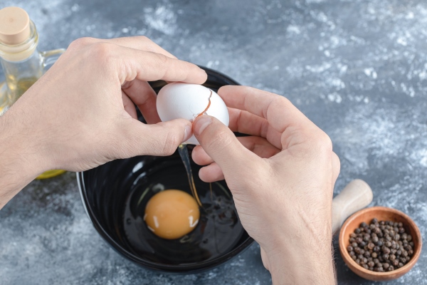 man hands breaking eggs in bowl over grey table - Драники с яйцом
