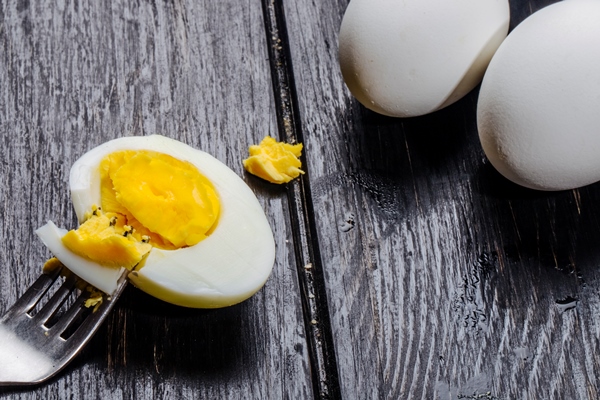 side view of boiled egg half with fork on wooden rustic - Фаршированные яйца с крабовыми палочками