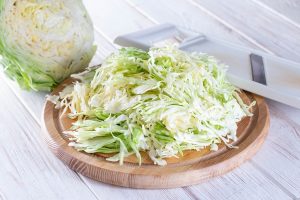 sliced fresh cabbage on a cutting board with a grater on a white wooden background - Наливной пирог с капустой