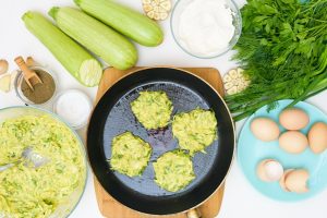 step by step recipe to cook pancakes of zucchini and greens on a light background with the addition of eggs flour garlic pepper the view from the top - Кабачковые оладьи