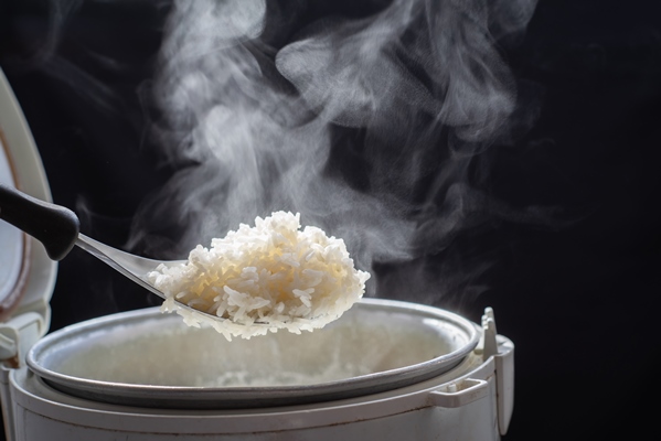 the steam from man taking tasty rice with spoon from cooker in kitchen jasmine rice cooking in electric rice cooker with steam selective focus - Бульон с рисом
