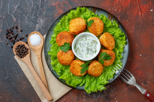 top view chicken nuggets lettuce fork on plate salt and black pepper in wooden spoons on dark table - Яичные котлеты по-карельски