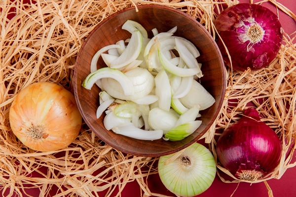 top view of sliced white onion in bowl with sweet red and whole white one on straw and red - Шурпа с нутом