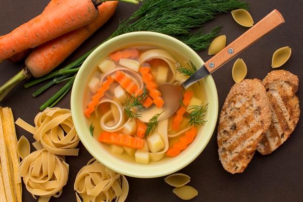 top view of winter vegetables soup in bowl with spoon and toast - Бульон с макаронными изделиями