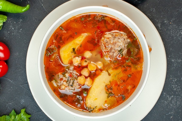 top view yummy meat soup with greens and seasonings on dark background - Шурпа с нутом