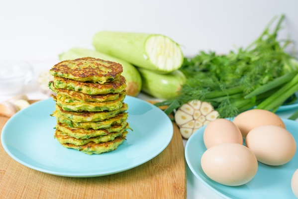 veggie fried pancakes with zucchini greens blue plate light background wooden board top view selective focus space - Кабачковые оладьи