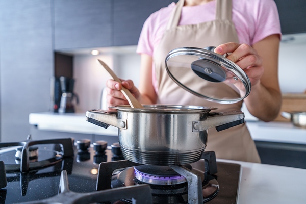 woman housewife in apron using steel metal saucepan for preparing dinner in the kitchen at home - Чай латте