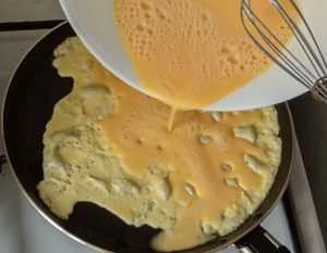 woman prepares an omelette on a gas stove - Омлет "Пуляр"