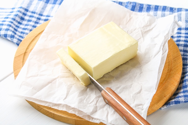 a bar of butter on a wooden board with a knife on a white table ingredients for cooking - Паштет из печени