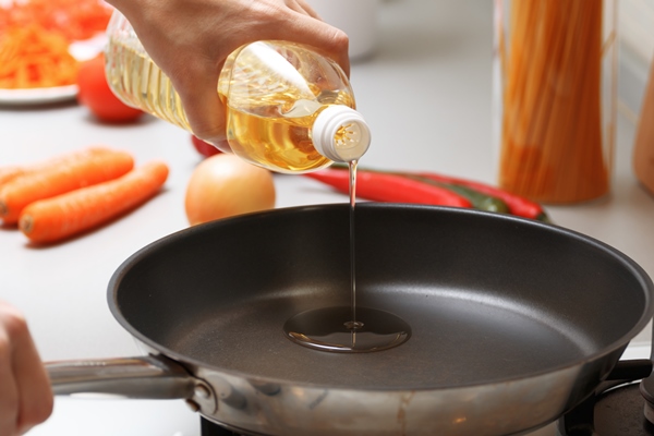 a woman pouring oil from a bottle into the pan in the kitchen near fresh vegetables and pasta - Рыбный суп-пюре
