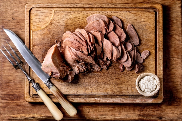 baked beef tongue sliced serving with horseradish sauce and meat knife on wooden cutting board over wood surface - Правила выбора и приготовления мяса