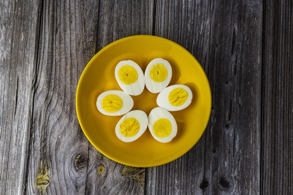 boiled egg halves in a yellow bowl on wooden table - Сельдь под шубой