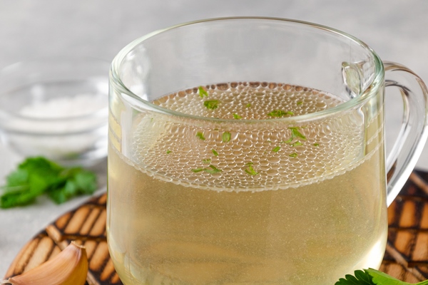 chicken broth in a glass cup with parsley garlic and other spices copy space - Ризотто