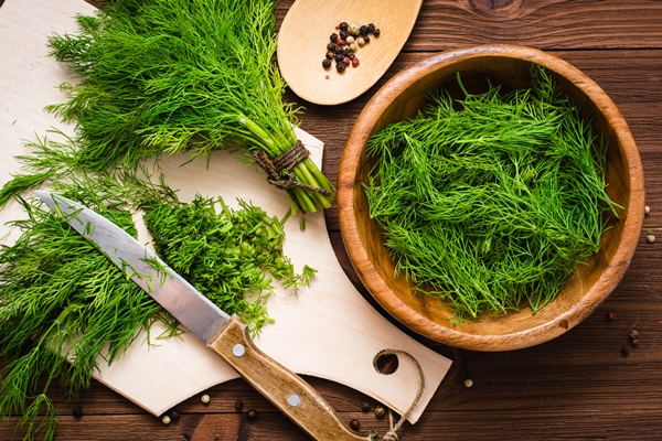 chopped fresh dill on a cutting board and dill in a wood bowl on the table top view - Молочный суп с лососем и рисом