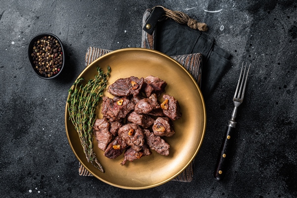 chopped grilled diced beef garlic steak on a plate with thyme black background top view - Тушёная говядина с картофелем и луком