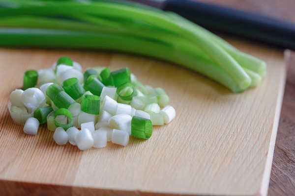 close up view on chopped fresh spring onion and knife put on wood cutting board - Картофельный салат с огурцами и яйцом