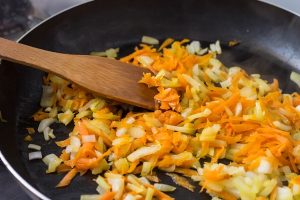 crushed onions and carrots in a frying pan and wooden spatula - Грибы с овощами под сырным соусом