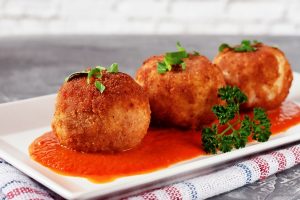 delicious hot italian arancini rice balls stuffed with cheese in tomato sauce in a plate on an old wooden table - Биточки рисовые