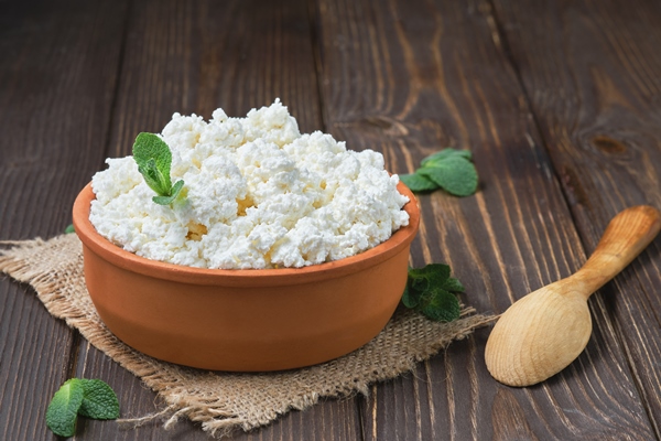 farmer s cottage cheese in a traditional clay bowl next to a wooden spoon a black wooden table - Галушки из творога