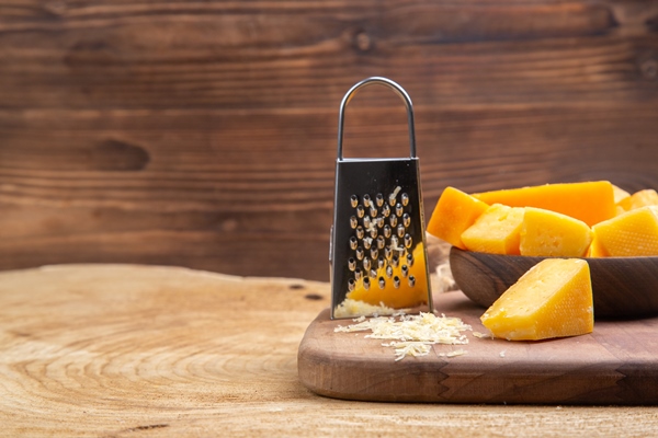 front view slices of cheese in wooden bowl grater on chopping board on wooden surface - Сырные крокеты