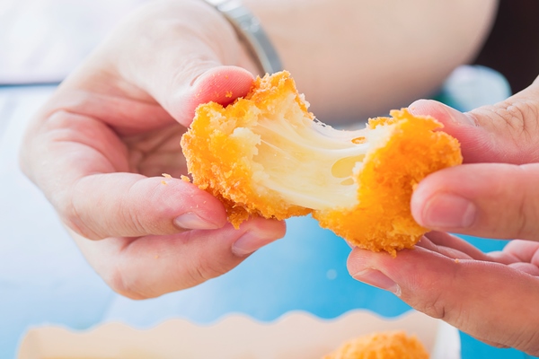 hand is holding a stretch cheese ball ready to be eaten with soft focused french fries - Сырные крокеты