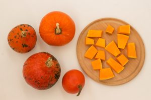 orange pumpkins on a white surface and sliced pumpkin on a cutting board - Молочный суп с тыквой и рисом
