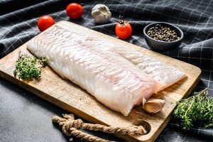 raw cod fillet with and herbs on rustic wooden cutting board black background top view - Паровое рыбное суфле